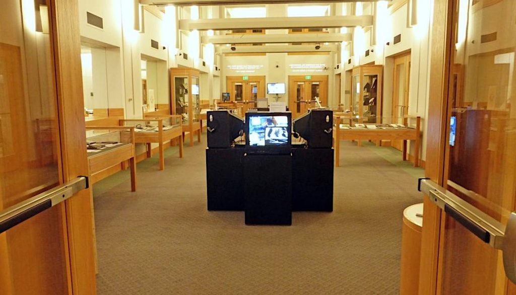 Signal to Code exhibition: a group of video monitors on stands in a hall of display cases