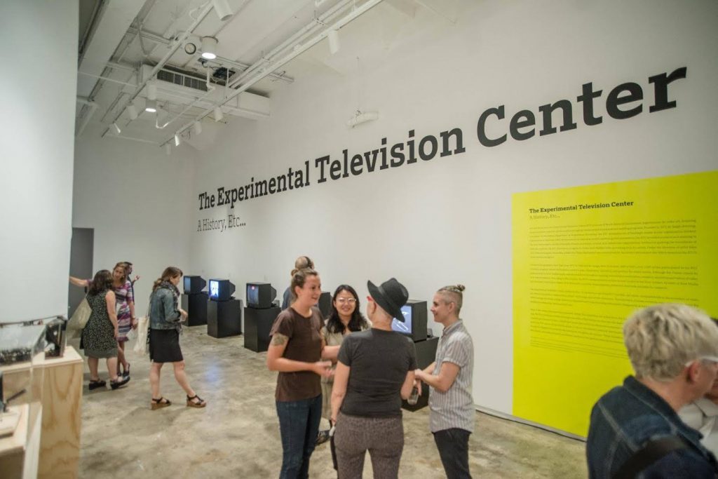 Visitors in the Hunter College gallery, below the exhibition title The Experimental Television Center