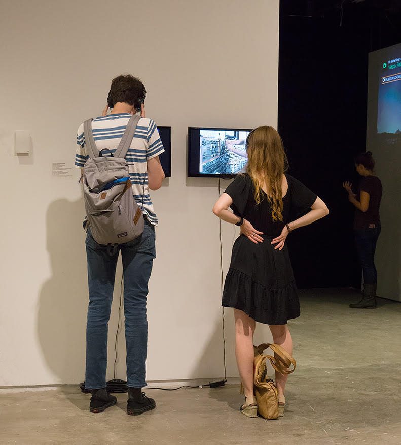 Two visitors watch video monitors on the gallery wall