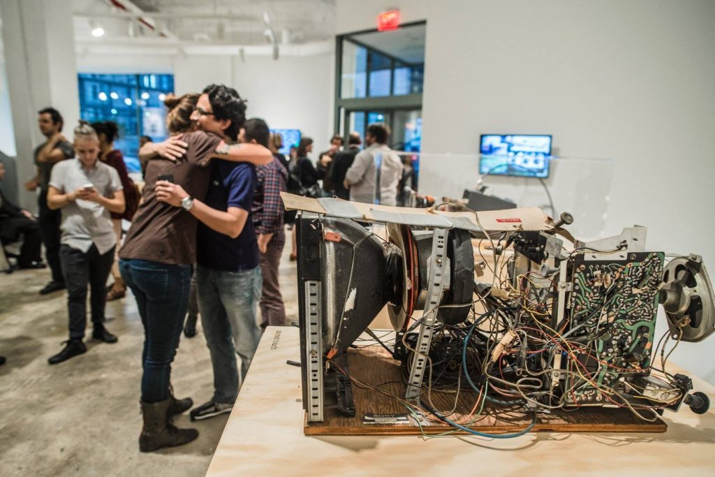 An old wobbulator, a television opened to its circuits, on show as visitors talk behind it